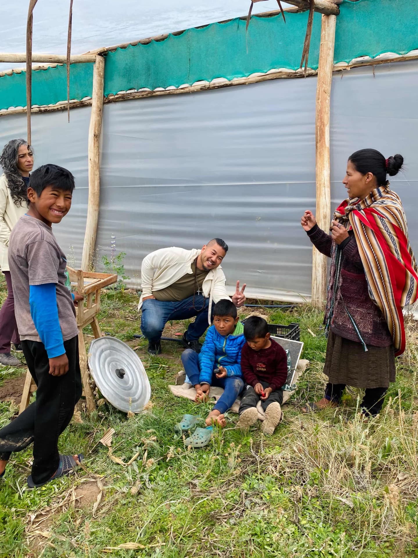 Zachary with a local family in a greenhouse in the Sacred Valley, children smiling beside him.
