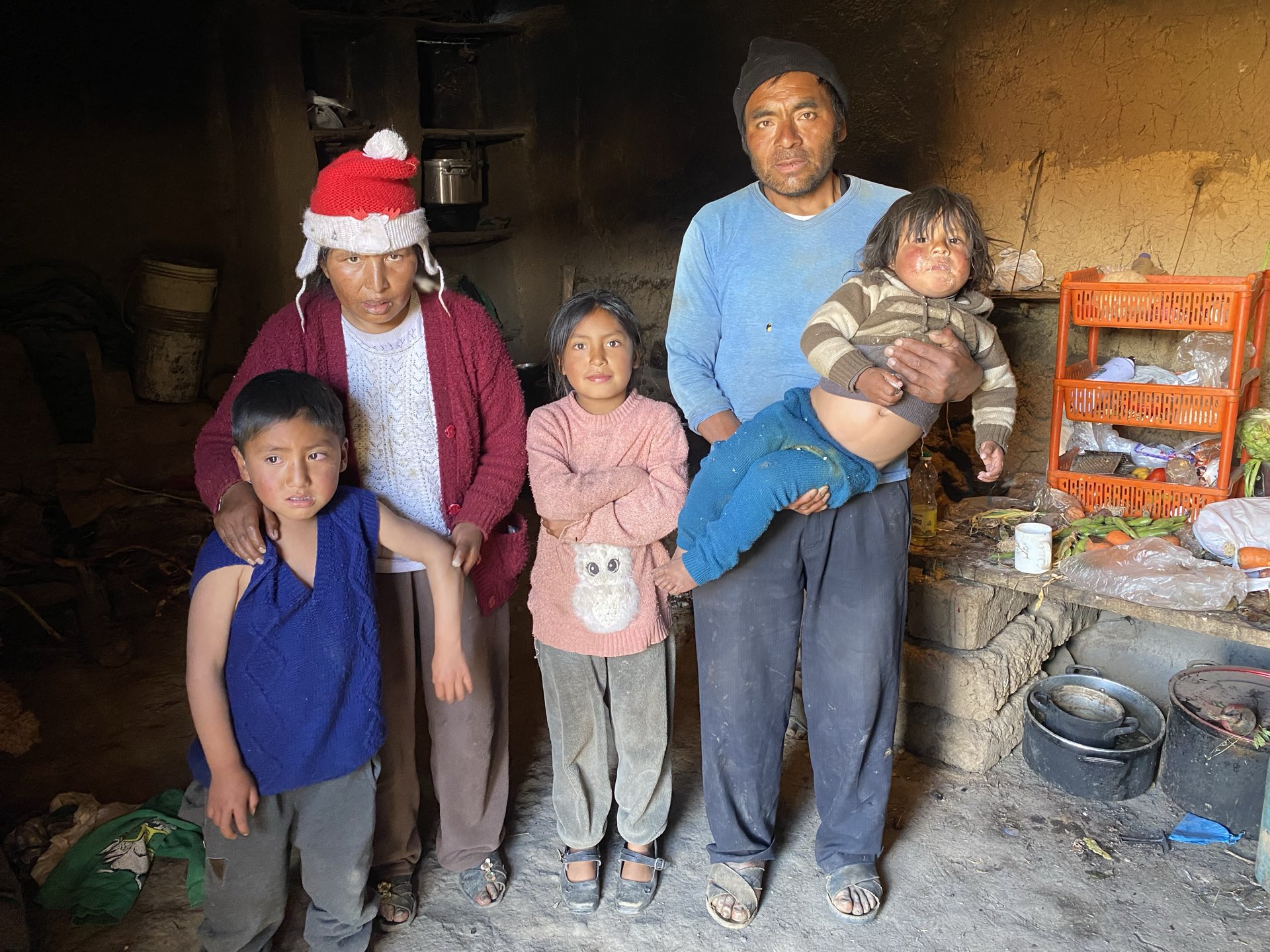 A family of six in their kitchen in the Sacred Valley, the father holding the youngest.